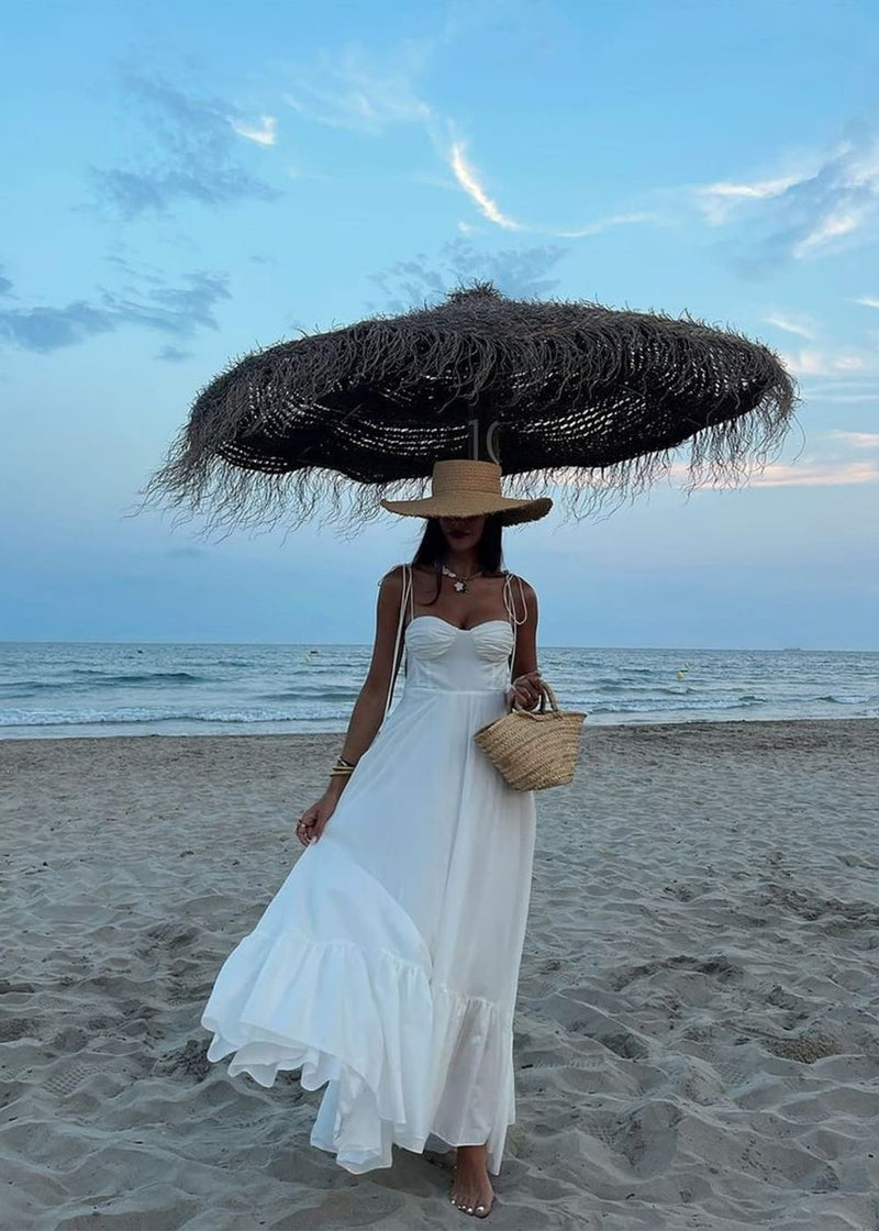 Mujer con vestido Aumare Èze blanco bajo sombrilla de playa